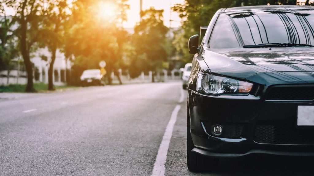 Carro estacionado em uma rua arborizada ao pôr do sol.