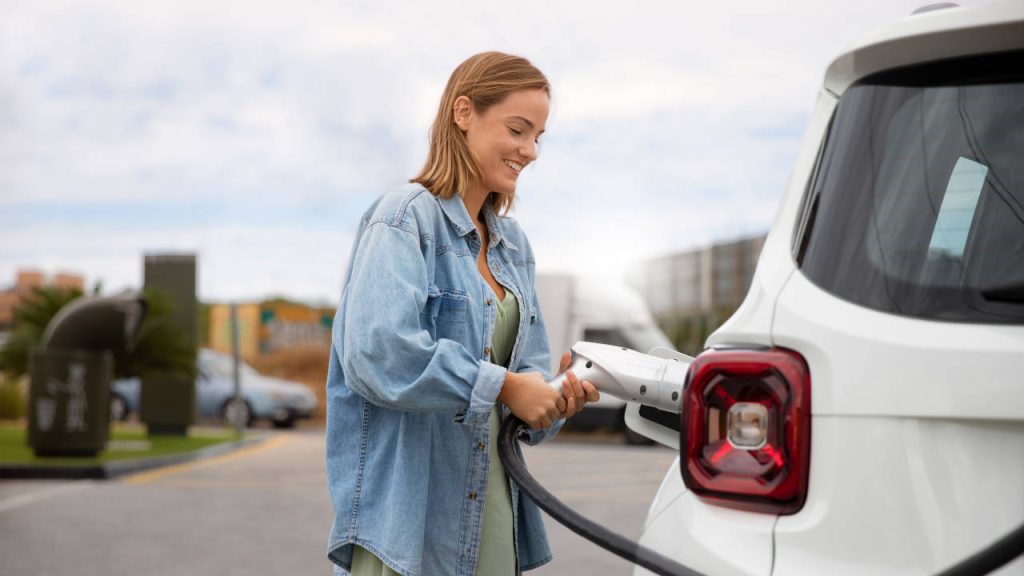 Mulher conectando um carro elétrico a uma estação de carregamento.