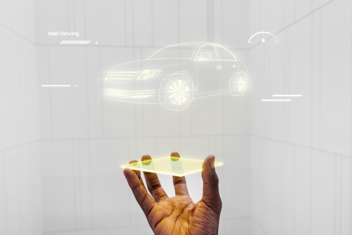 Uma mão segurando um dispositivo transparente com um holograma de carro flutuando acima dele, representando tecnologia avançada de realidade aumentada e inovação automotiva.