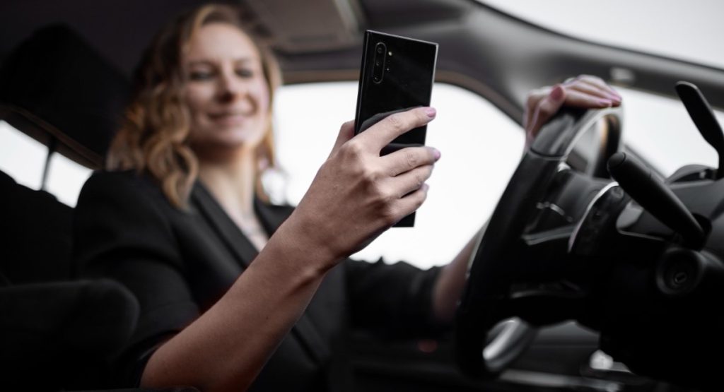 Mulher sorridente segurando smartphone enquanto dirige.