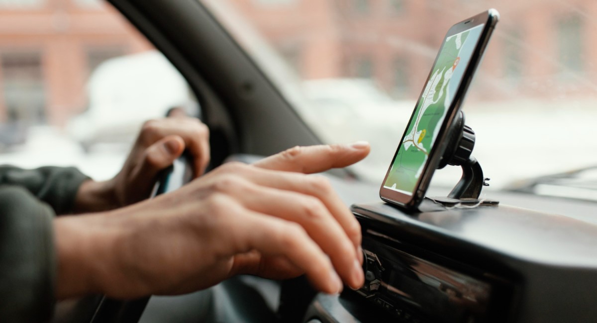 Motorista ajustando GPS no smartphone montado no painel do carro.