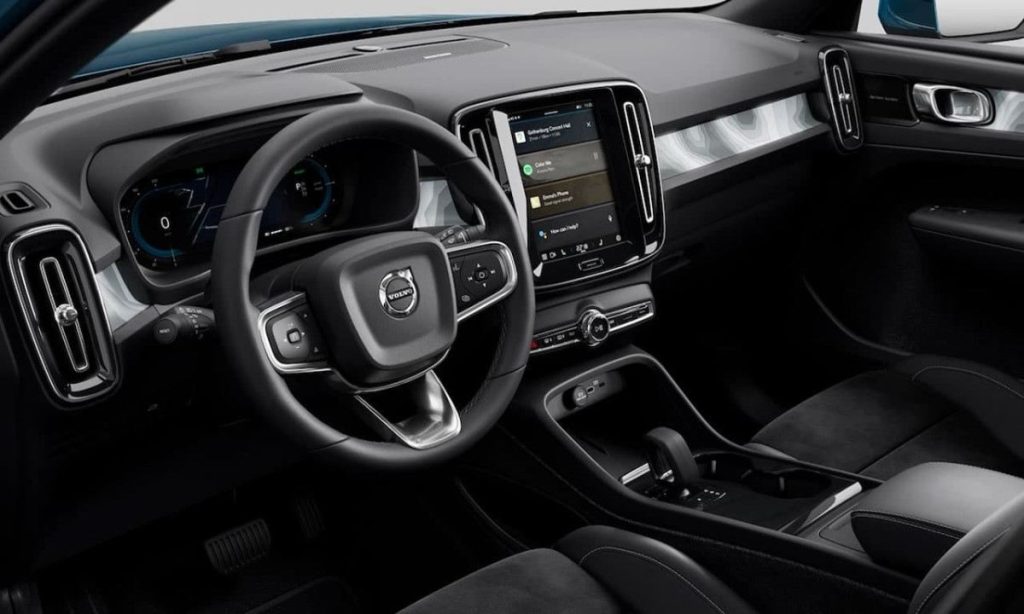 Imagem do interior do Volvo XC40, mostrando o painel de controle moderno com uma grande tela sensível ao toque, volante multifuncional, acabamentos em preto e assentos de couro.